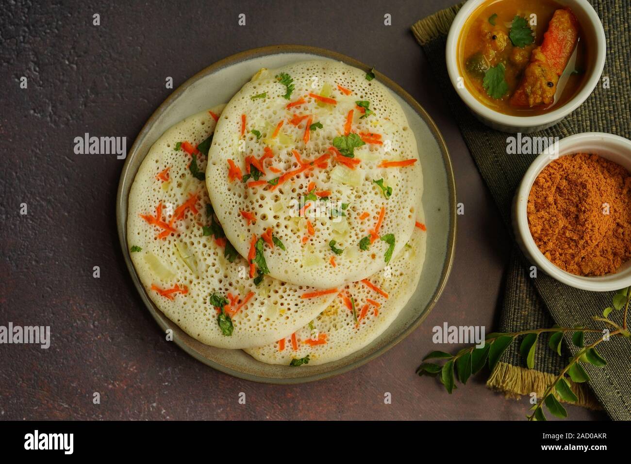 Uthappam/Oothappam - South Indian Frühstück set Dosa gekrönt mit Zwiebel Karotten mit Chutney Pulver und Sambar serviert. Stockfoto