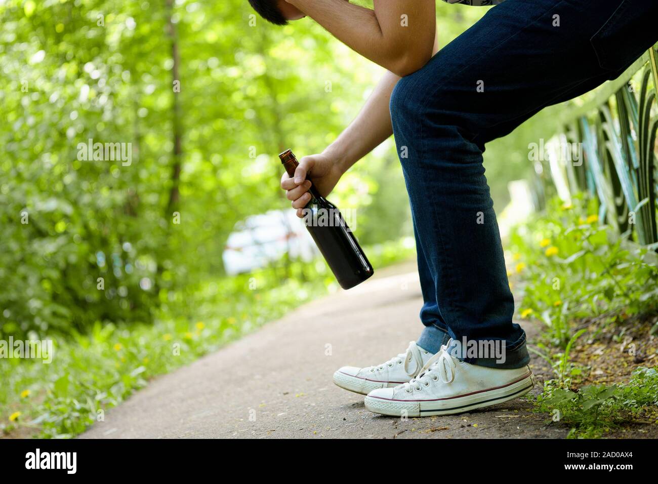 Mann mit Bierflasche auf grünen Zaun im Freien sitzen deprimiert. Stockfoto