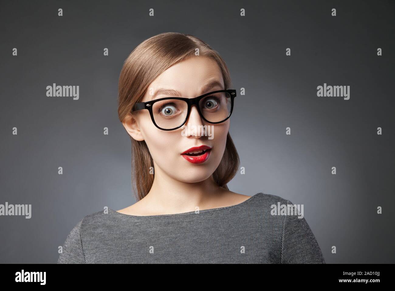 Mit weit aufgerissenen Augen erstaunt Frau auf grauem Hintergrund Stockfoto