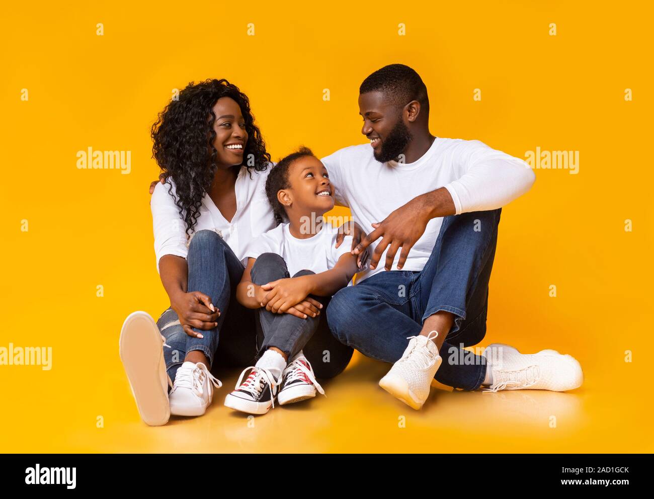 Schwarze Eltern umarmt mit ihren adopred Tochter, auf dem Boden sitzen zusammen Stockfoto