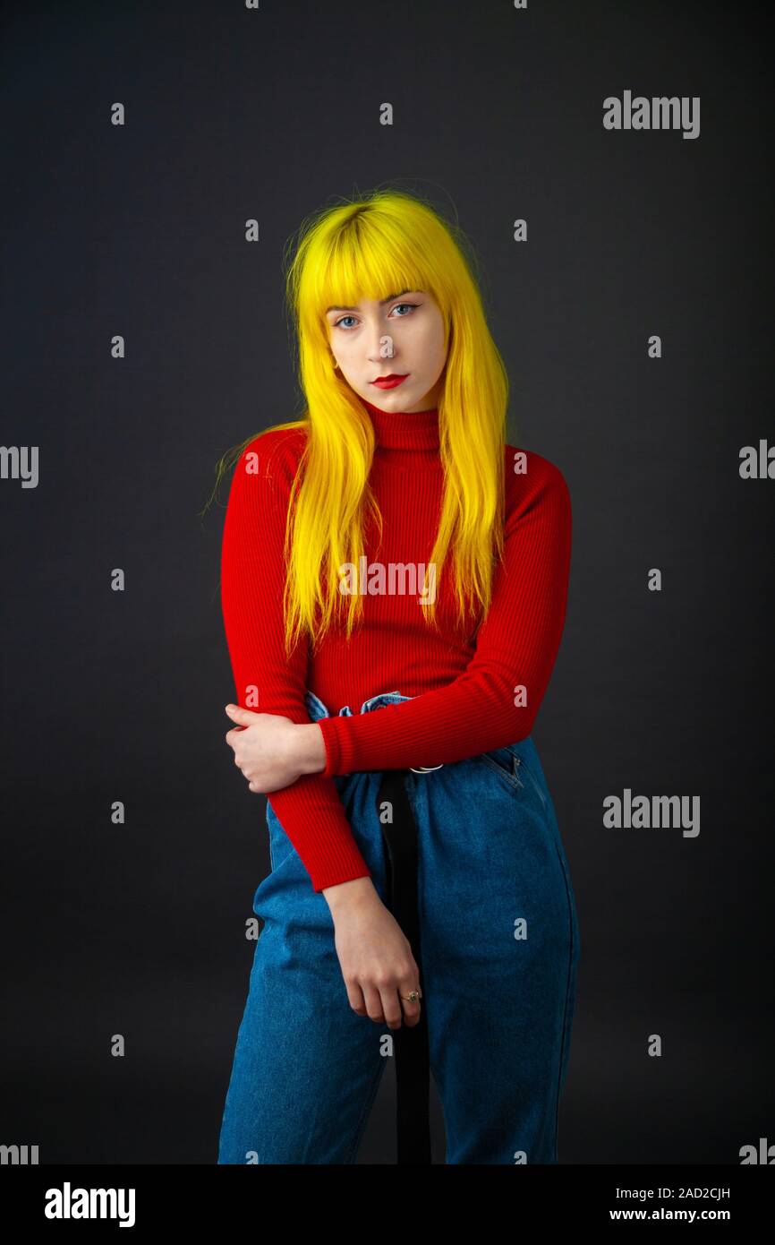 Eine junge Frau mit leuchtend gelben Haar zu tragen ein helles Rot langärmeliges Oberteil auf einen einfachen dunklen Hintergrund. Stockfoto