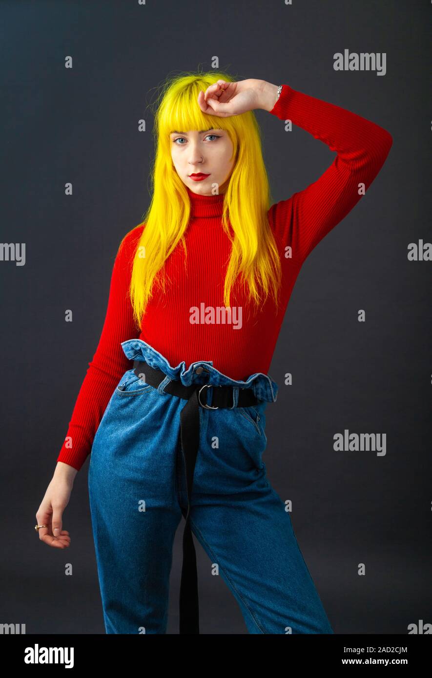 Eine junge Frau mit leuchtend gelben Haar zu tragen ein helles Rot langärmeliges Oberteil auf einen einfachen dunklen Hintergrund. Stockfoto