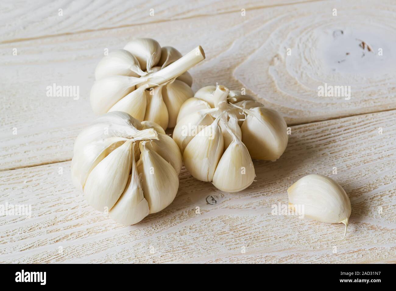 Drei Köpfe von rohem Knoblauch und eine Zehe auf einem weißen Holztisch. Würzig kochen Zutat. Vitamin gesunde Ernährung. Gemüse und Vegetarisch. Ansicht von oben. Stockfoto