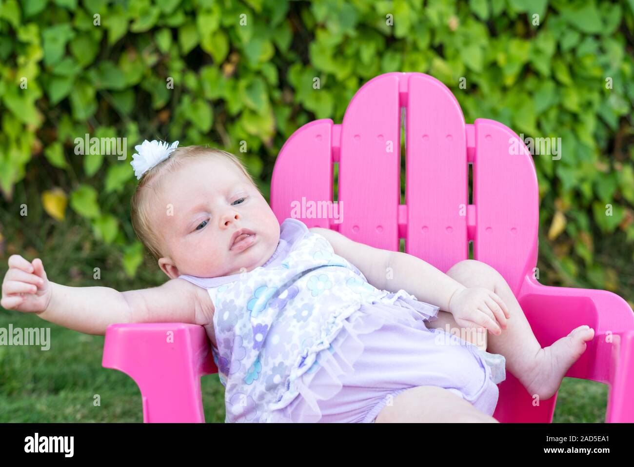 Baby Mädchen versucht, im Stuhl, draußen zu sitzen und beuge Stockfoto