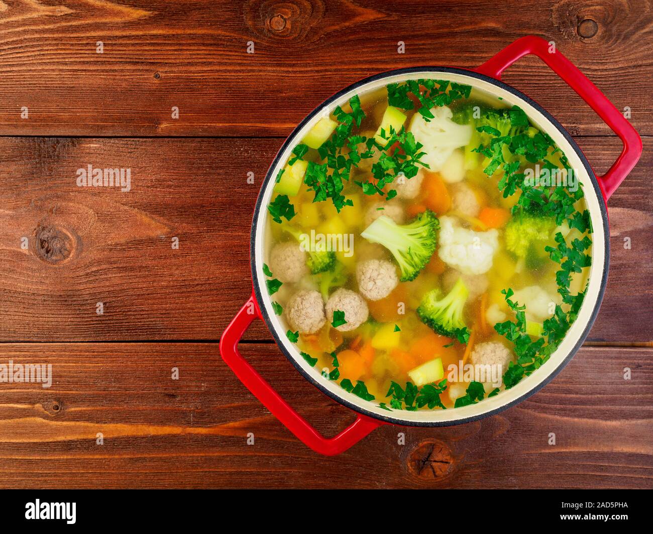 Große Metal cast rot Pan mit köstlichen heißen Suppe mit Gemüse und Frikadellen, Blumenkohl, Brokkoli, Möhren, Paprika, Kartoffeln, gesunde Diät essen. Br Stockfoto