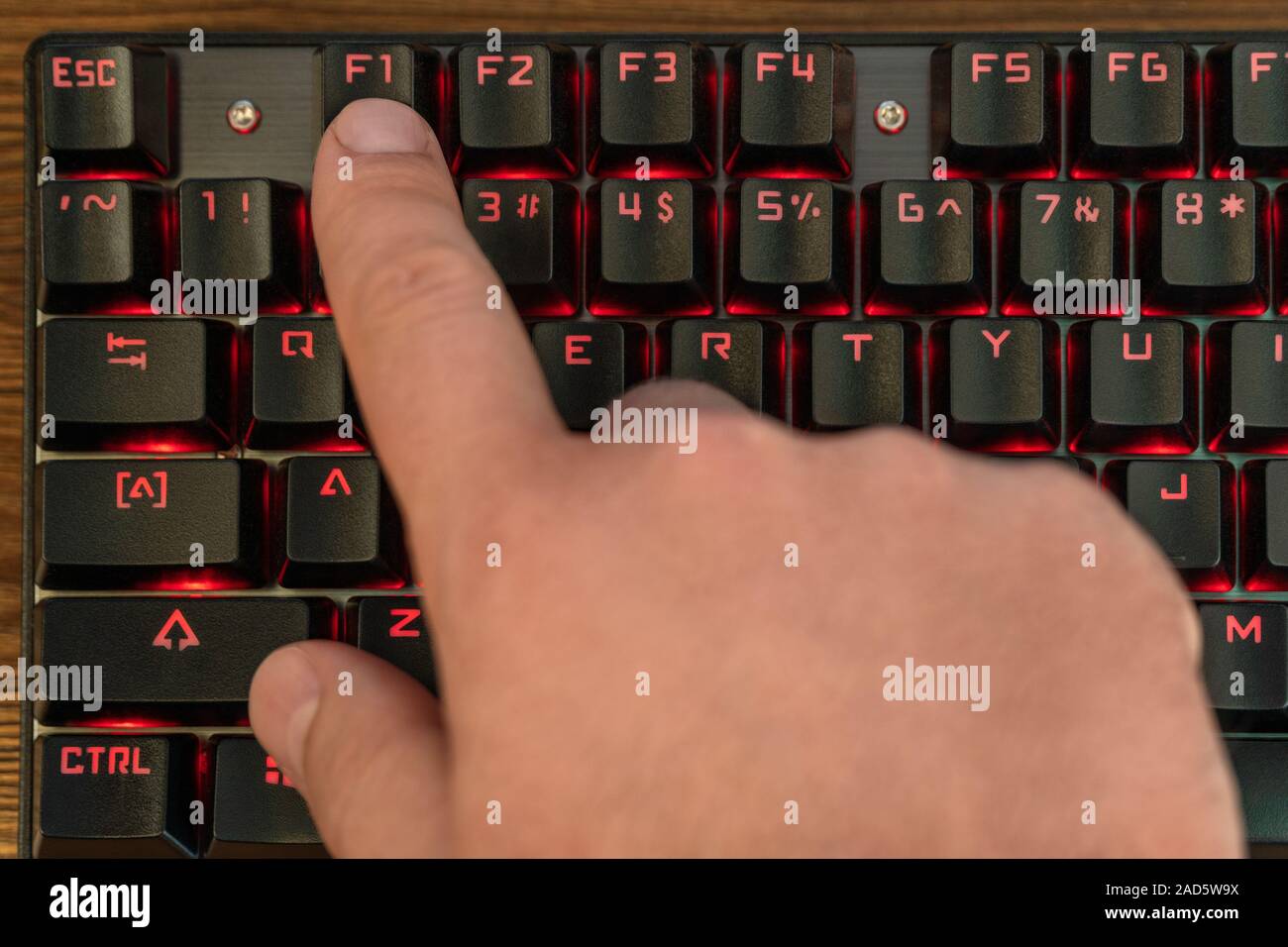 Männliche hand drückt die Taste F1 auf der Tastatur, schwarz mit roter Hintergrundbeleuchtung Stockfoto