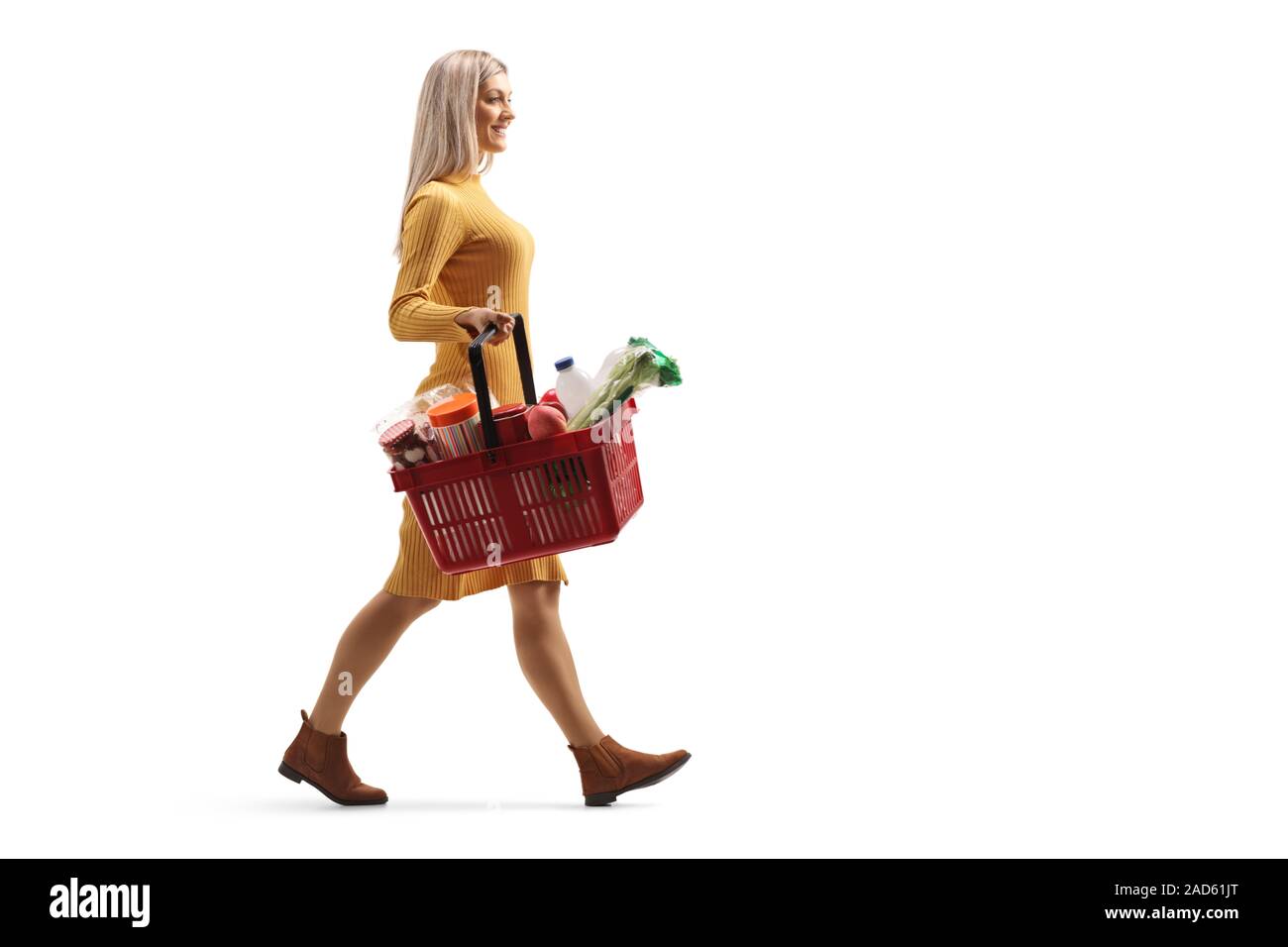 Volle Länge Profil geschossen von einer jungen Frau zu Fuß mit einem Warenkorb mit Lebensmitteln auf weißem Hintergrund Stockfoto