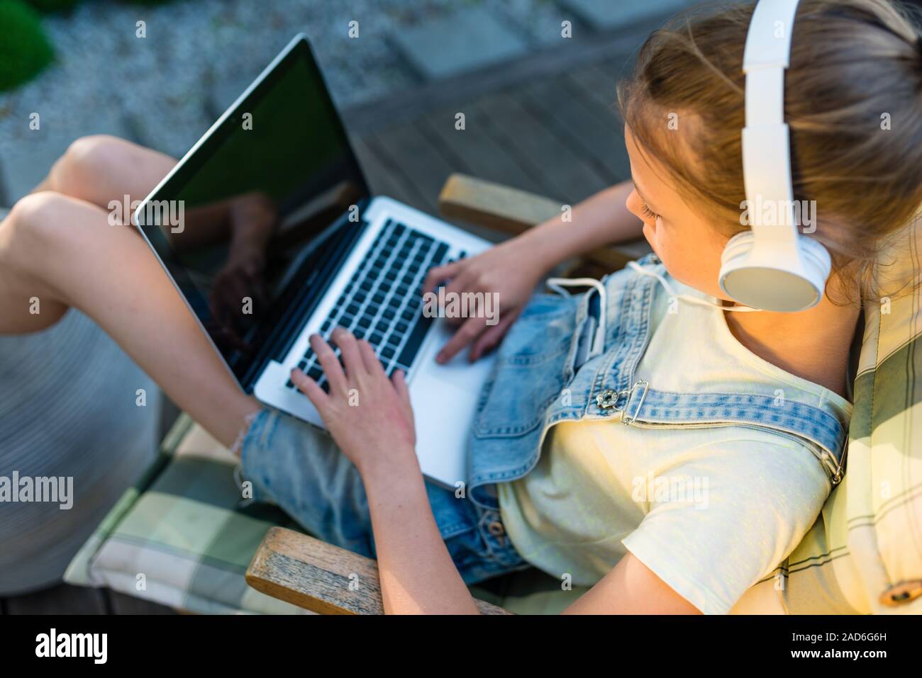 Recht jugendlich Mädchen im Kopfhörer hört Musik mit einem Laptop und sitzen draußen auf der Terrasse im Garten Stockfoto