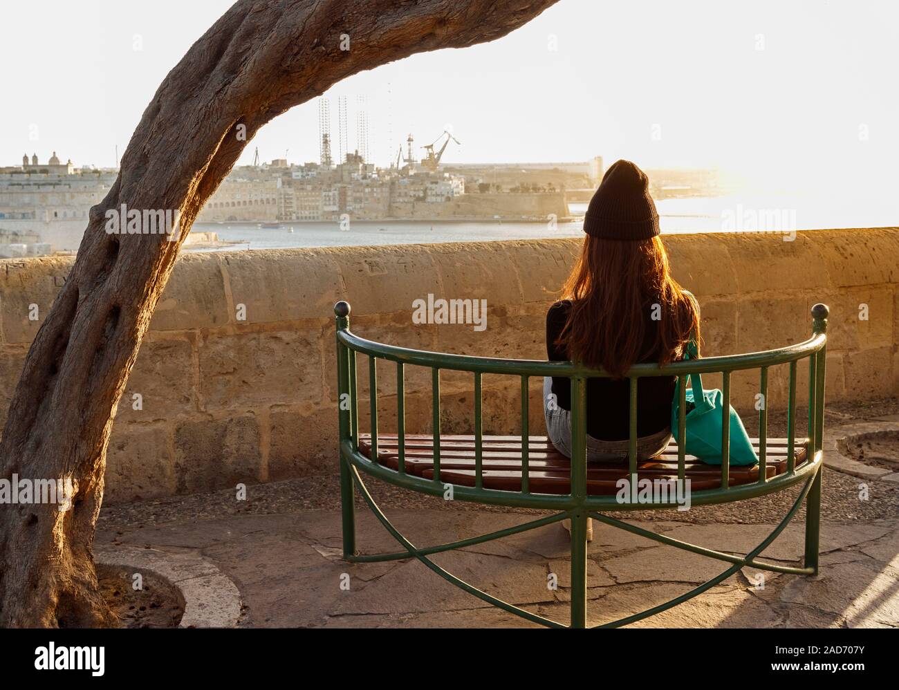 Junge Frau auf einer Bank am unteren Barrakka Gärten mit Blick auf den Grand Harbour in Valletta, Malta sitzen. Stockfoto