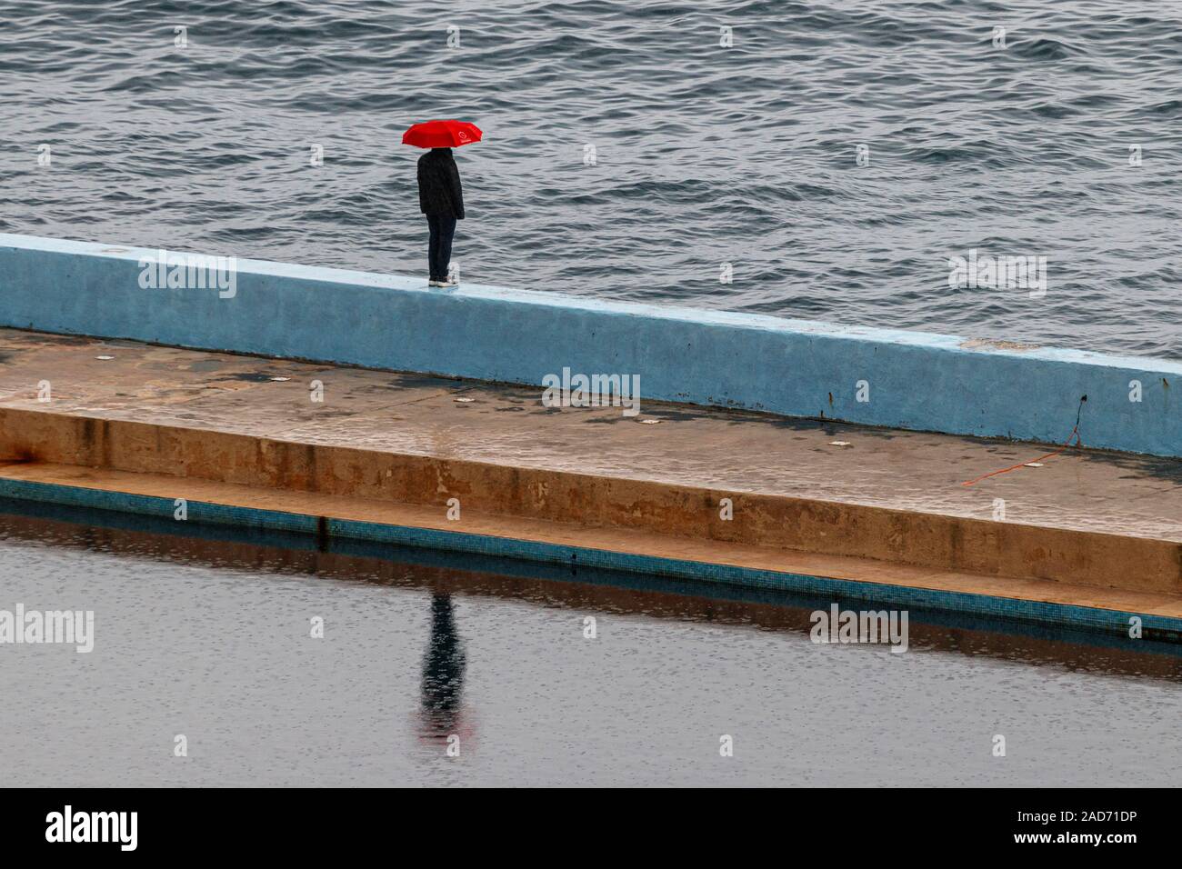 Person, die mit einem roten Regenschirm im Regen, am Meer-Wand in Sliema auf Malta. Stockfoto