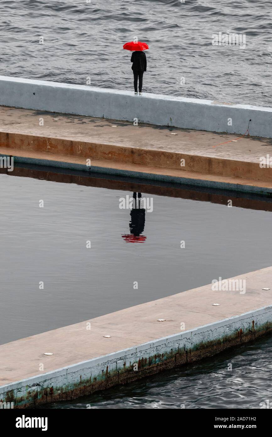 Person, die mit einem roten Regenschirm im Regen, am Meer-Wand in Sliema auf Malta. Stockfoto