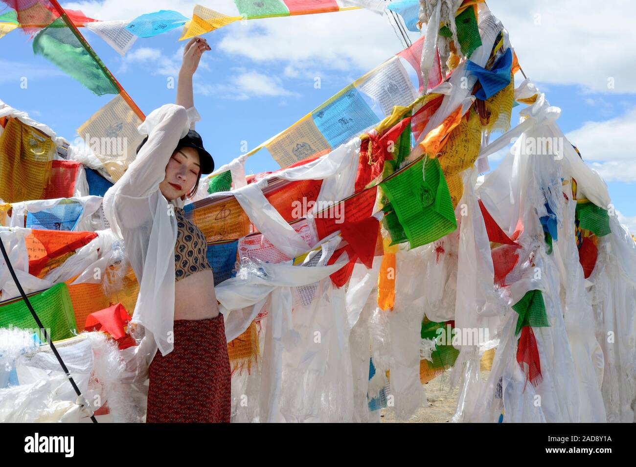 Eine junge Asiatin wirft inmitten Schichten von Gebetsfahnen und weißen Schal khatas in den Wind in Gampa Pass in der Autonomen Region Tibet der Volksrepublik China. Stockfoto