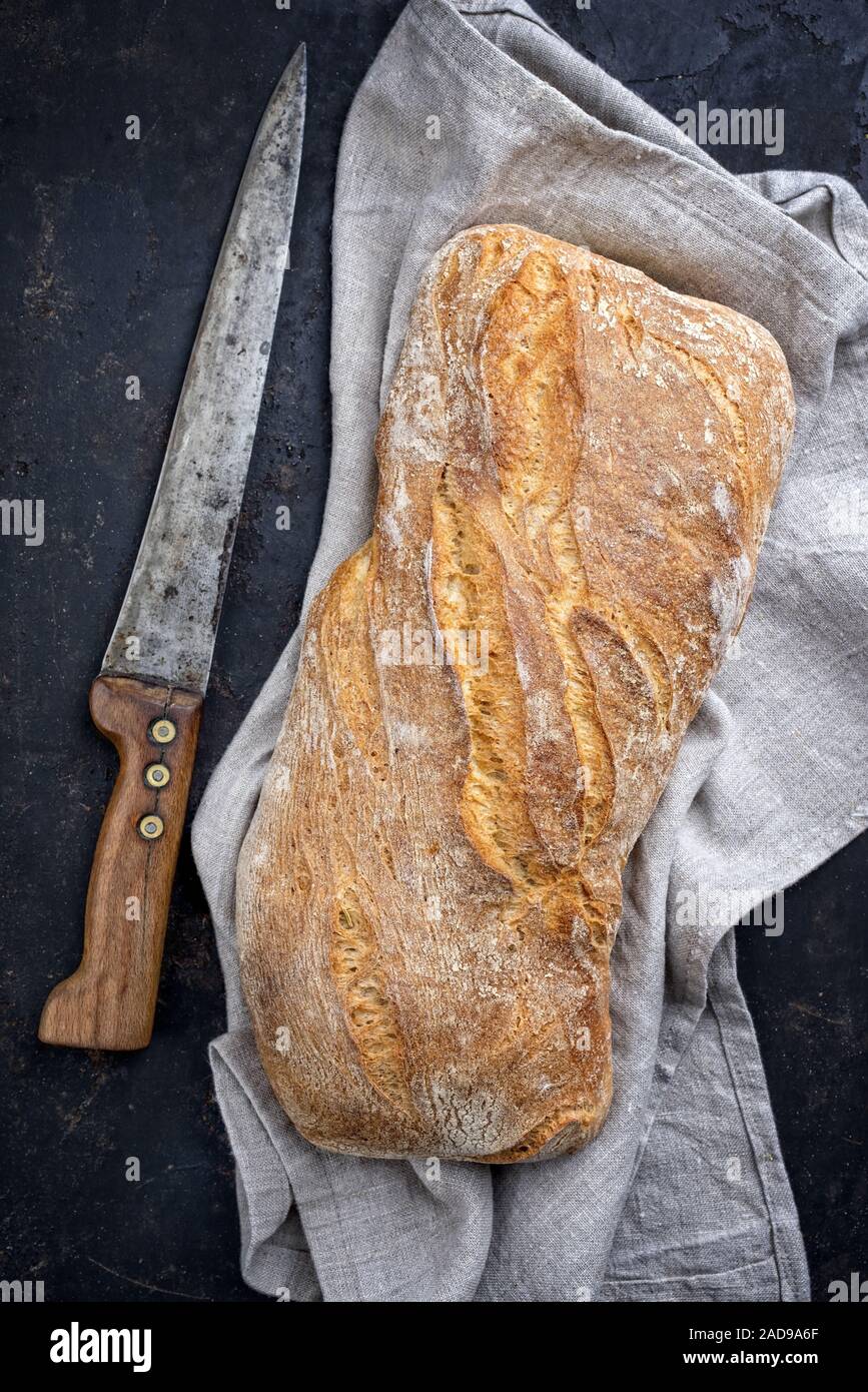 Traditionelle italienische Ciabatta Brot als Draufsicht auf ein altes Schwarzes Brett mit Messer Stockfoto