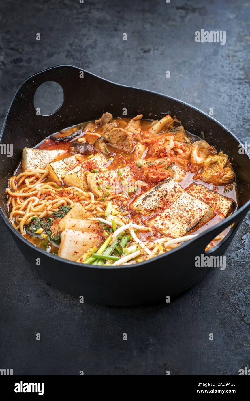 Traditionelles koreanisches Kimchi jjigae mit gegrillter Schweinebauch und Ramen als closeup in modernem Design Japanische gusseiserne Rösten dis Stockfoto