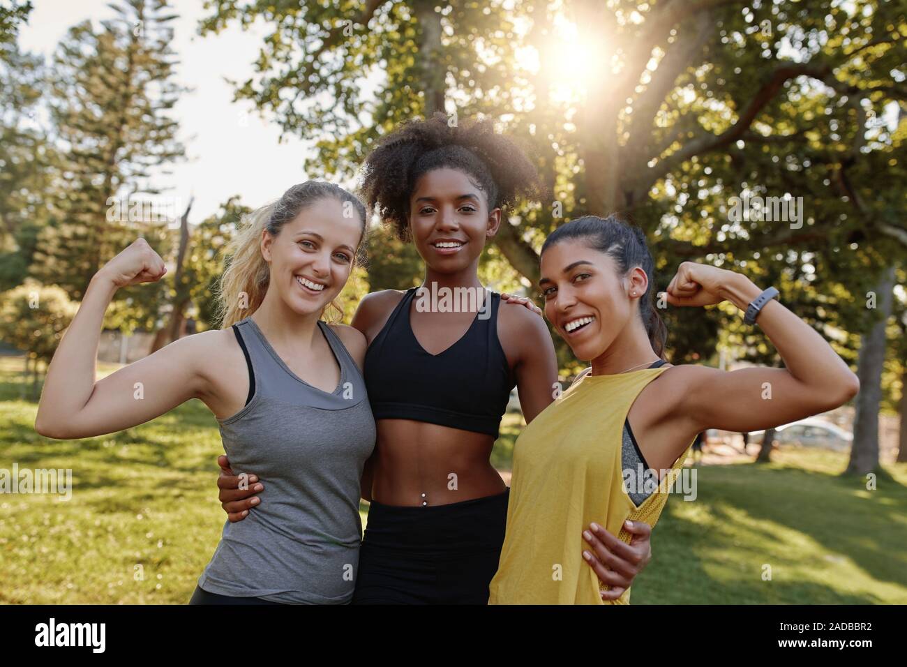 Portrait einer afrikanischen amerikanischen weiblichen stehende Frau mit ihren beiden unterschiedlichen Freunde ihre Muskel biegen im Park - 3 Frau zeigt Stärke und Stockfoto