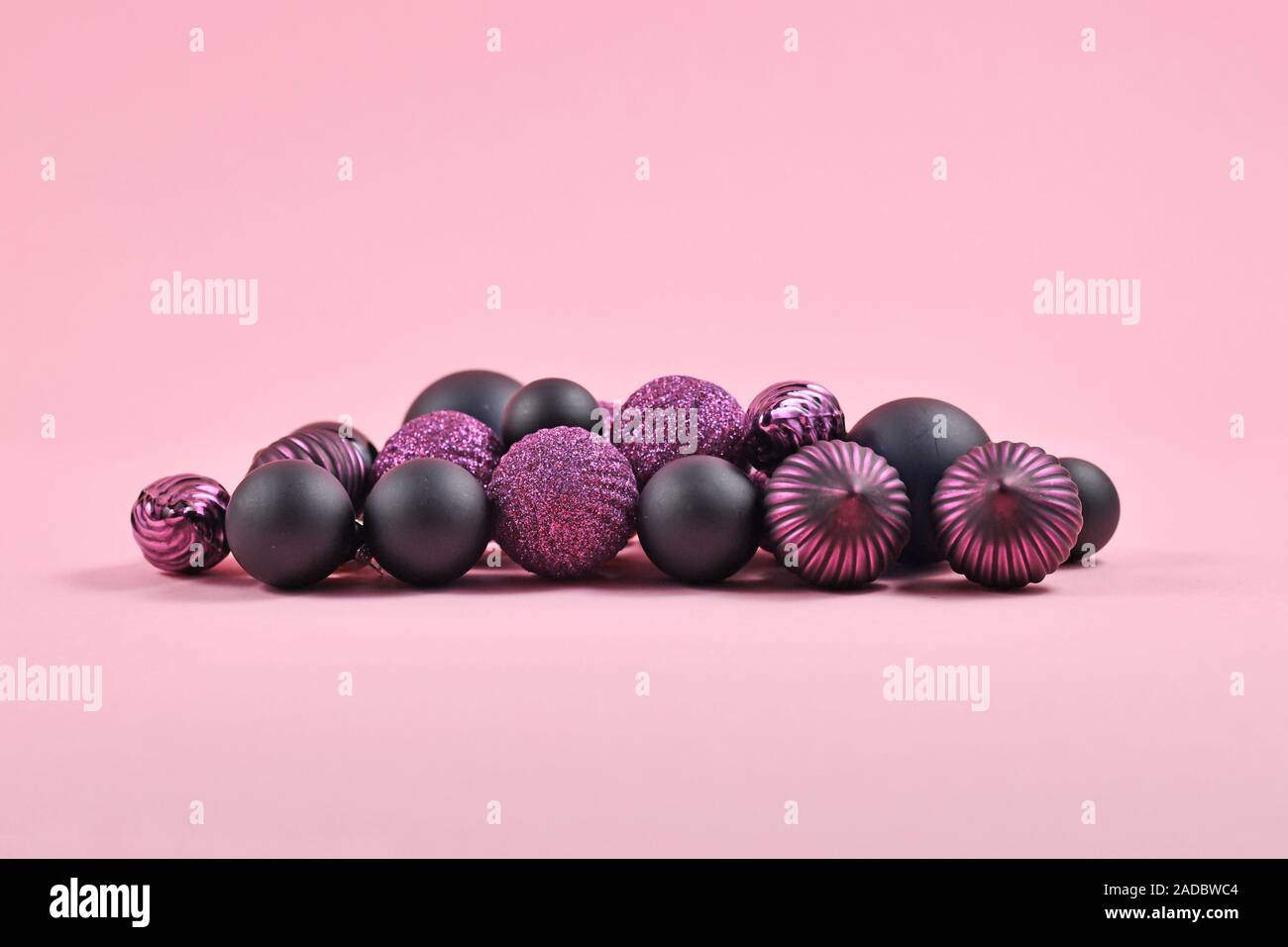 Stapel der dunkel Lila und Schwarz Christbaumschmuck in Form von runden Kugel Kugeln auf rosa Hintergrund Stockfoto