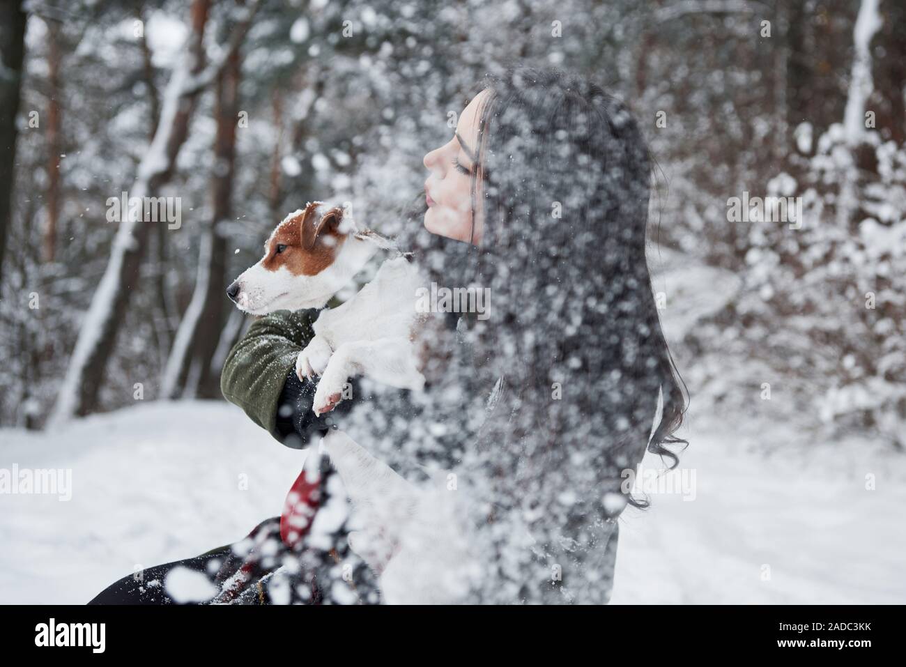 Es ist Schneefall. Smiling brunette Spaß beim Spaziergang mit ihrem Hund im Winter Park Stockfoto