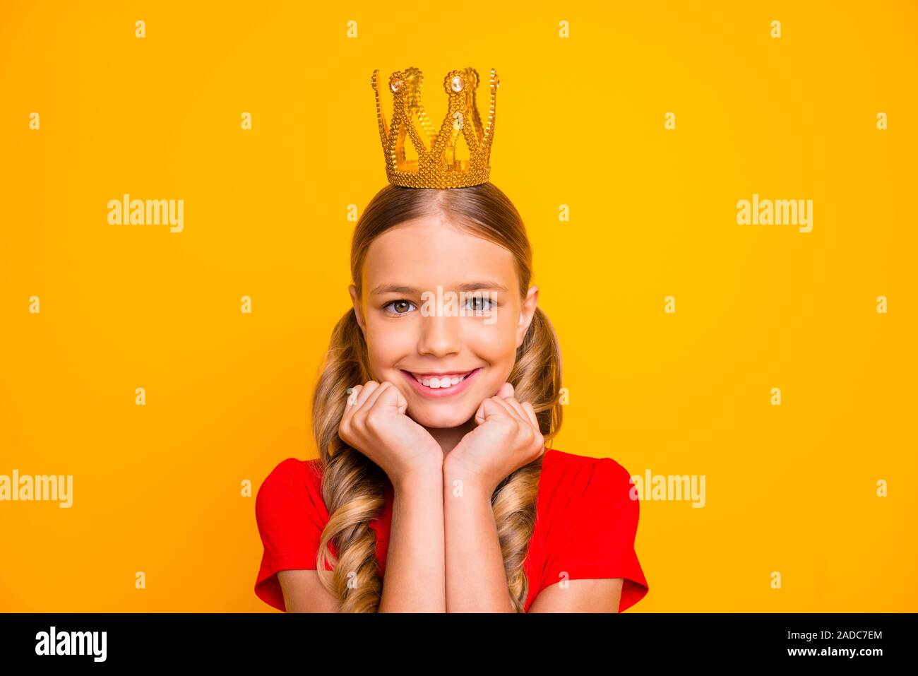 Foto des hübschen kleinen verträumten lady Arme auf die Wangenknochen Golden Tiara Kopf zufrieden gute Laune berühmte Person tragen Casual rotes T-Shirt isolierte Helle Stockfoto