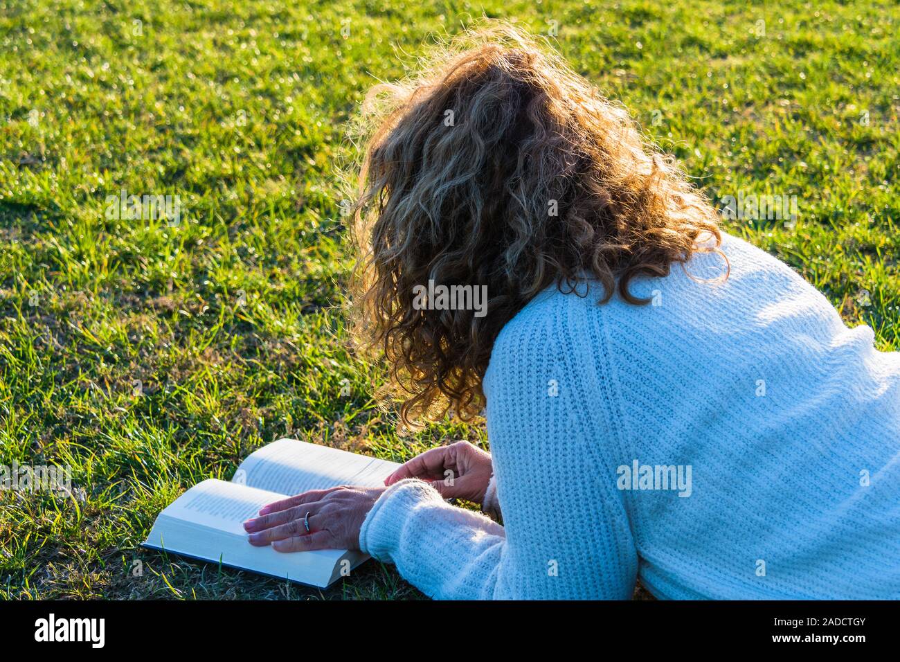 Blonde und lockig behaarte Frau liest im Park Stockfoto