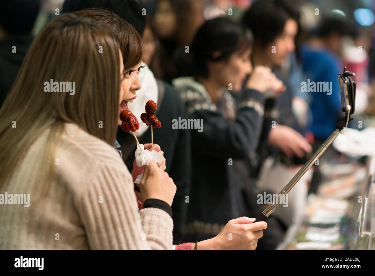 Kyoto, Japan - 03.November 2018: Zwei Frauen, die eine selfie Holding ein Tako tamago brochette an Nishiki Markt in Kyoto. Tako tamago ist eine beliebte Straße Stockfoto