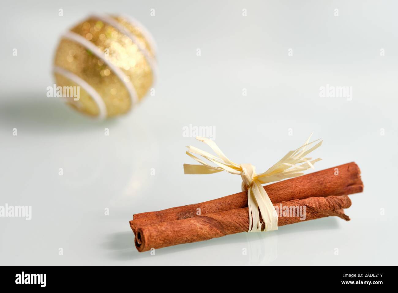 Helle noch Leben mit einer Nahaufnahme von Cinnamon Sticks mit einem Bogen auf einem weißen Glasplatte und einem goldenen Christbaumkugel im Hintergrund Stockfoto