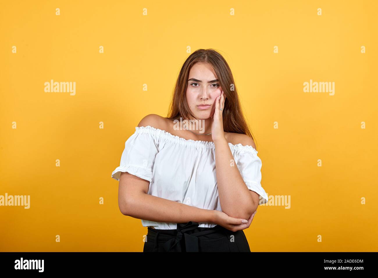 Ernsthafte junge Frau an der Kamera suchen, die Hand auf die Wange auf orange Wand Stockfoto