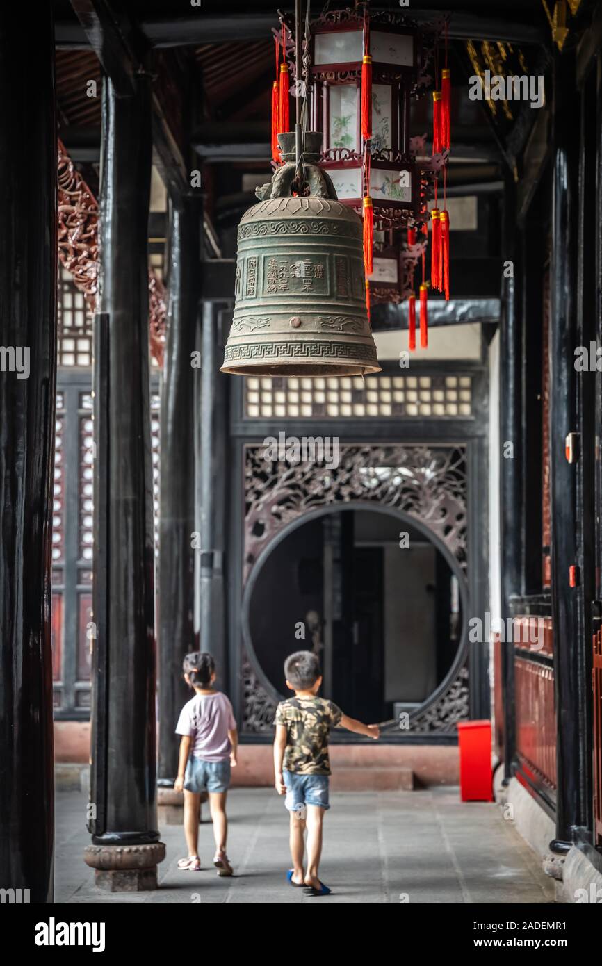 Chengdu, China - Juli 2019: Zwei kleine Jungs gehen unter der großen Messing Glocke unter dem Dach in Wenshu Kloster hängen Stockfoto