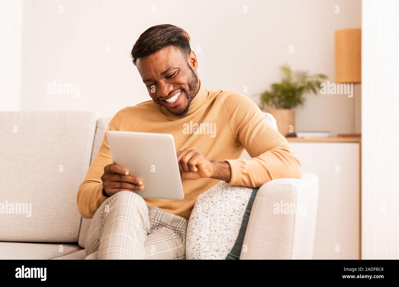 Schwarze Kerl mit Tablet lächelnd Sitzen auf einem Sofa zu Hause Stockfoto