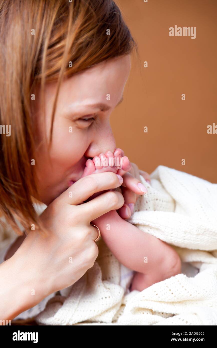 Home Portrait von Mutter, Hände halten und küssen ihr Kind, süßes neugeborenes Baby Rosa süße Füße in weißen Decke. Konzept lange erwarteten Sohn, IVF, Cesar Stockfoto