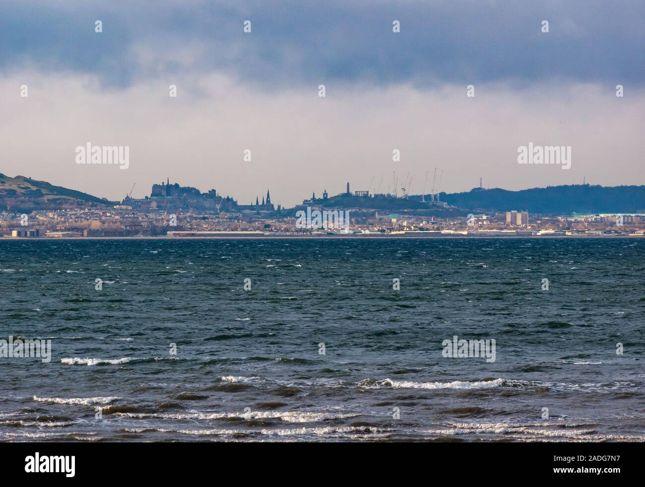 Longniddry Bents, East Lothian, Schottland, Vereinigtes Königreich, 4. Dezember 2019. UK Wetter: ein Dunkler bedrohlicher Himmel breitet sich über die Skyline von Edinburgh an einem windigen Tag mit Arthur's Seat, Edinburgh Castle, Calton Hill Denkmäler und die hohe Kräne der St James Sanierung Bau Arbeit sichtbar. Blick von longniddry Bents über die Firth fo Her Stockfoto