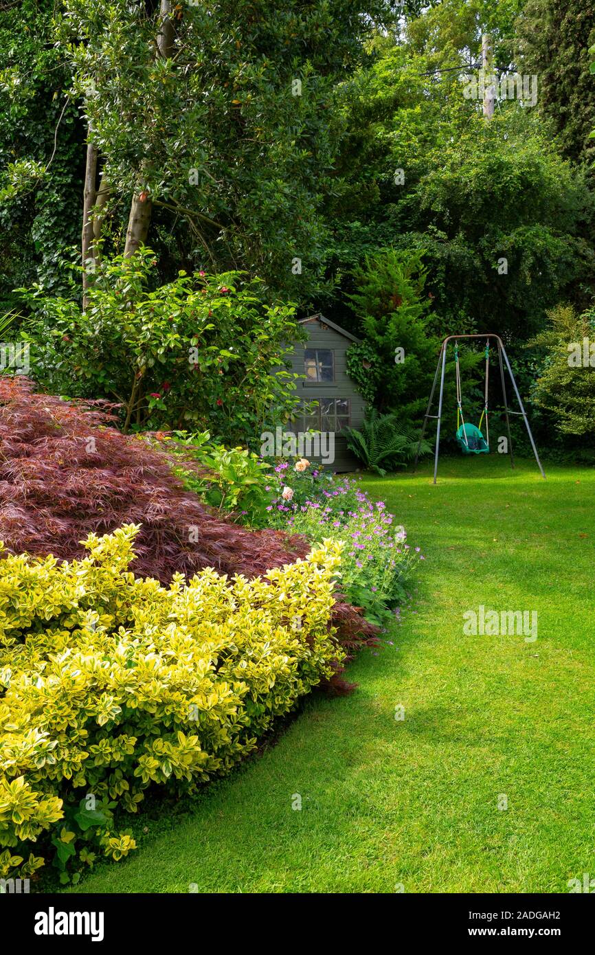 Blick auf abfallenden Garten mit Blumenrabatten. Mit Euonymus undulata