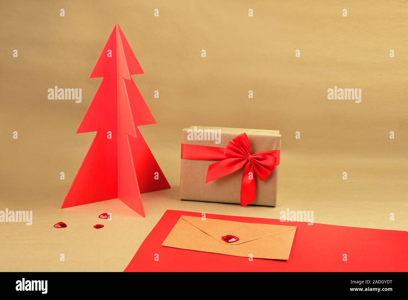 Geschenkbox und Umschlag mit rotem Holz Weihnachtsbaum auf einem natürlichen braunen Hintergrund mit verstreuten Herzen. Stockfoto