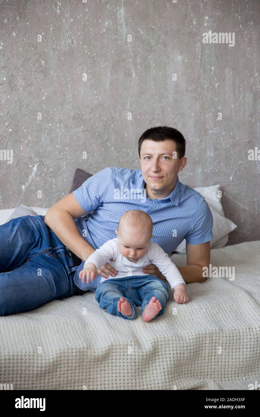 Glückliche Junge kaukasier Familie im Studio. Vater ist das Halten und umarmte seine Tochter in den Händen. Man liegt auf dem Bett. Mann lächelnd. Für Kleinkinder ist ernst. Co Stockfoto