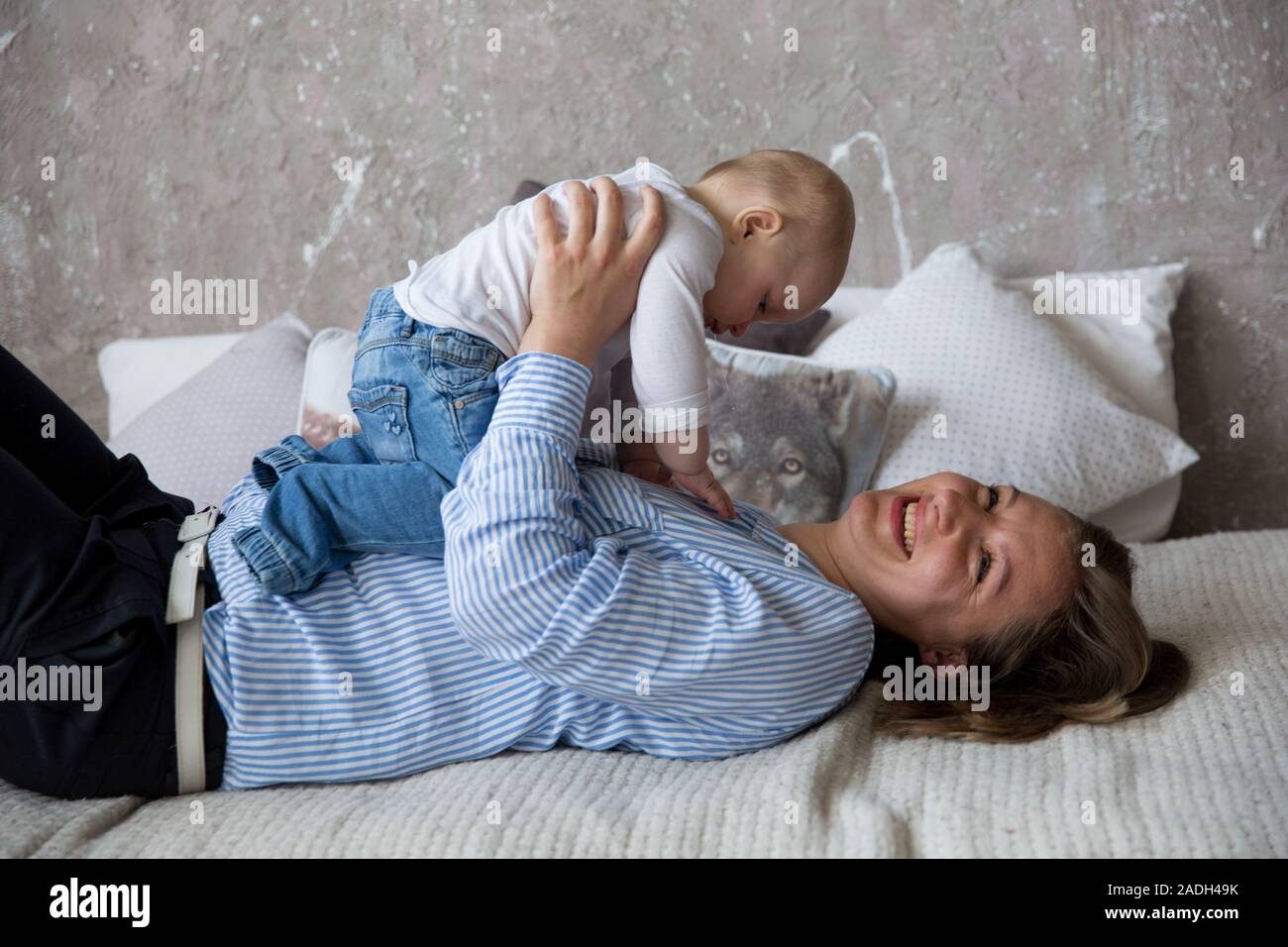 Glückliche Junge kaukasier Familie im Studio. Mutter halten und umarmte seine Tochter in den Händen. Liegende Frau auf dem Bett. Frau lächelnd. Kleinkind liegen auf M Stockfoto