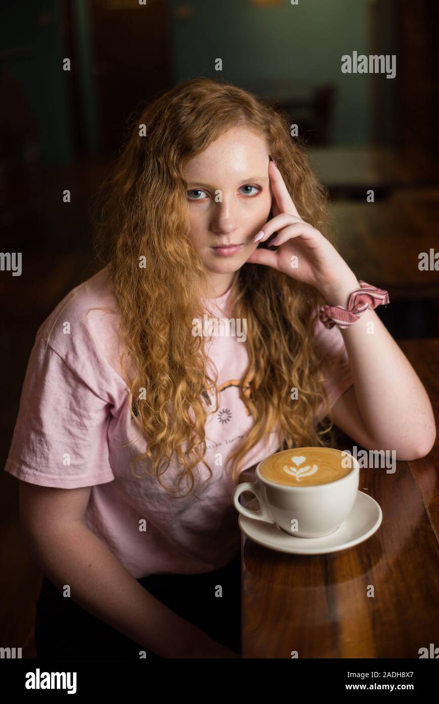 Eine rothaarige Mädchen an einem Tisch sitzen mit einer Tasse Kaffee. Stockfoto