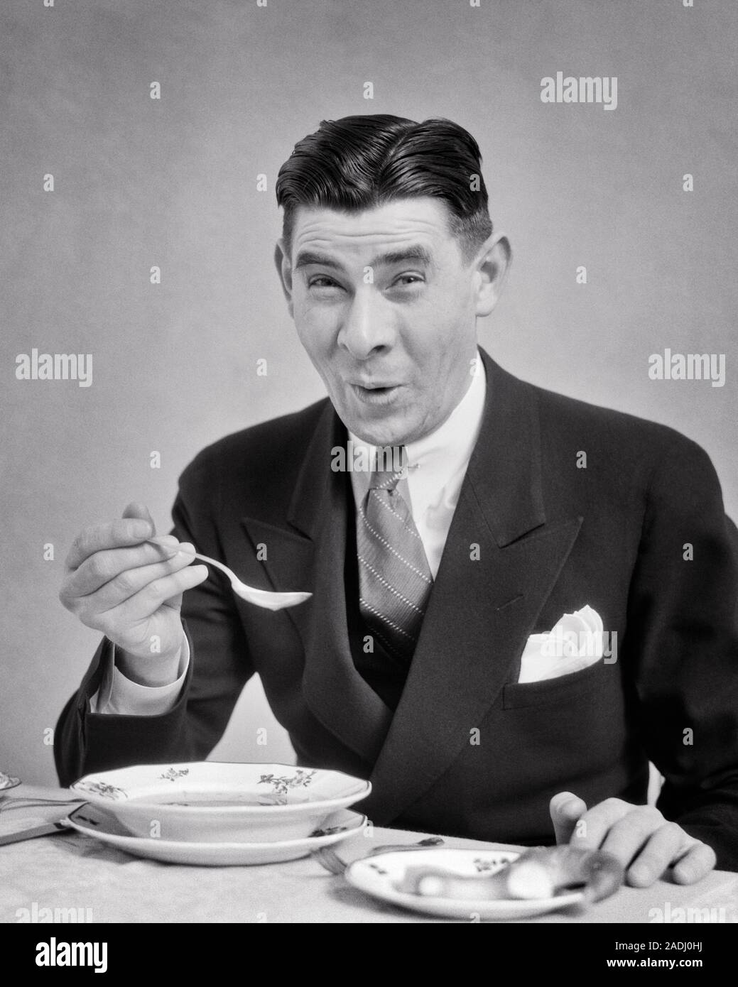 1930er Jahre Mann mit Anzug und Krawatte essen eine Schüssel mit Suppe, einen lustigen GESICHTSAUSDRUCK als Suppe ZU HEISS ODER LECKER ODER SCHRECKLICH - f 5856 HAR 001 HARS KOPIE RAUM MIT HALBER LÄNGE PERSONEN MÄNNER AUSDRÜCKE B&W AUGENKONTAKT BRUNETTE Anzug und Krawatte humorvoll und Aufregung Ernährung komische Geschmack lecker konzeptionelle Komödie konsumieren, konsumieren Nahrung stilvolle schrecklich oder schlechten Geschmack Mitte - Mitte - erwachsenen Mann SCHWARZ UND WEISS KAUKASISCHEN ETHNIE KÖSTLICHE HAR 001 ALTMODISCH Stockfoto