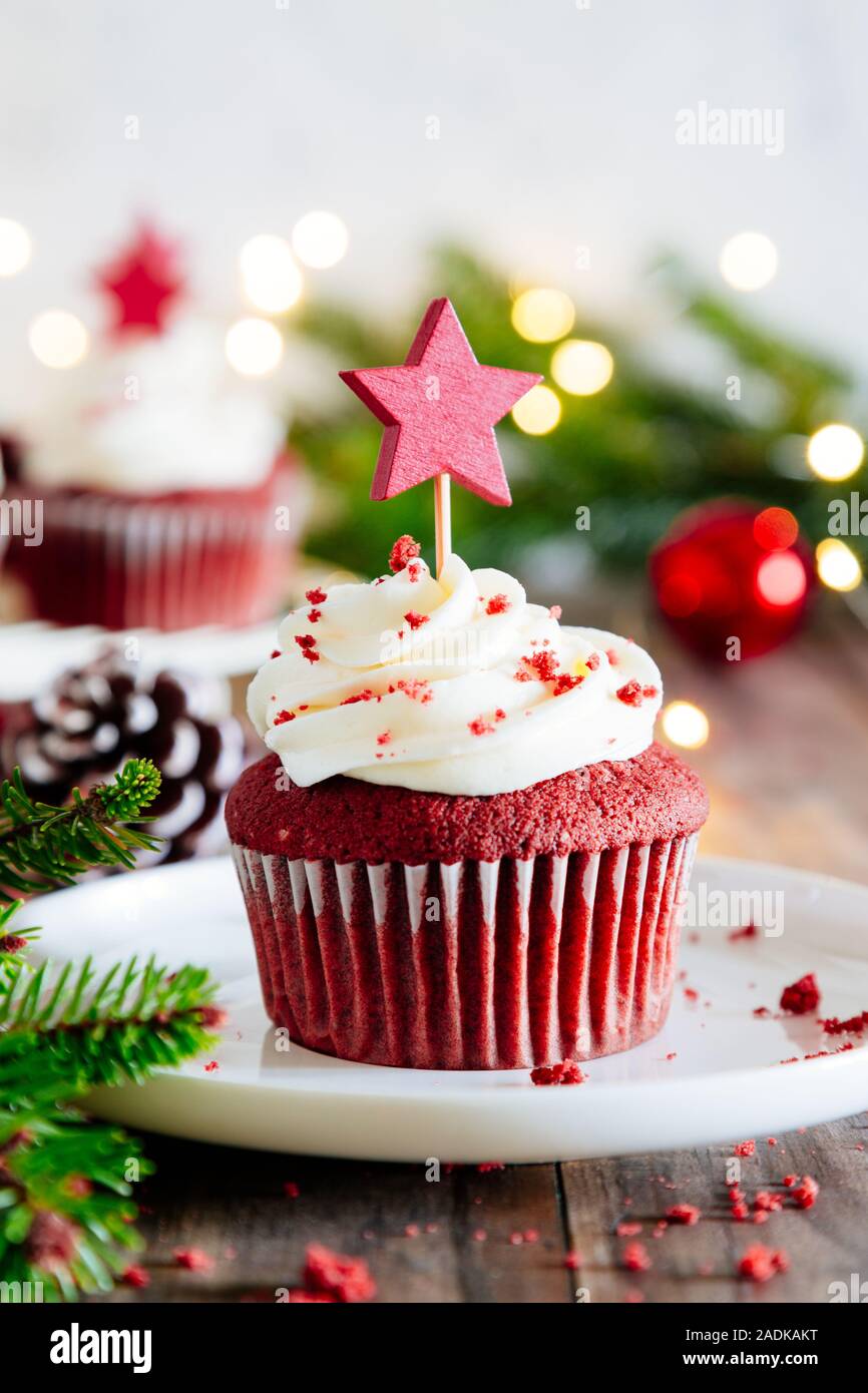 Weihnachten red velvet Cupcakes mit einem sternförmigen Kuchen abholen dekoriert, mit Weihnachtsschmuck, Tanne und Lichtern auf einem rustikalen Holztisch Stockfoto