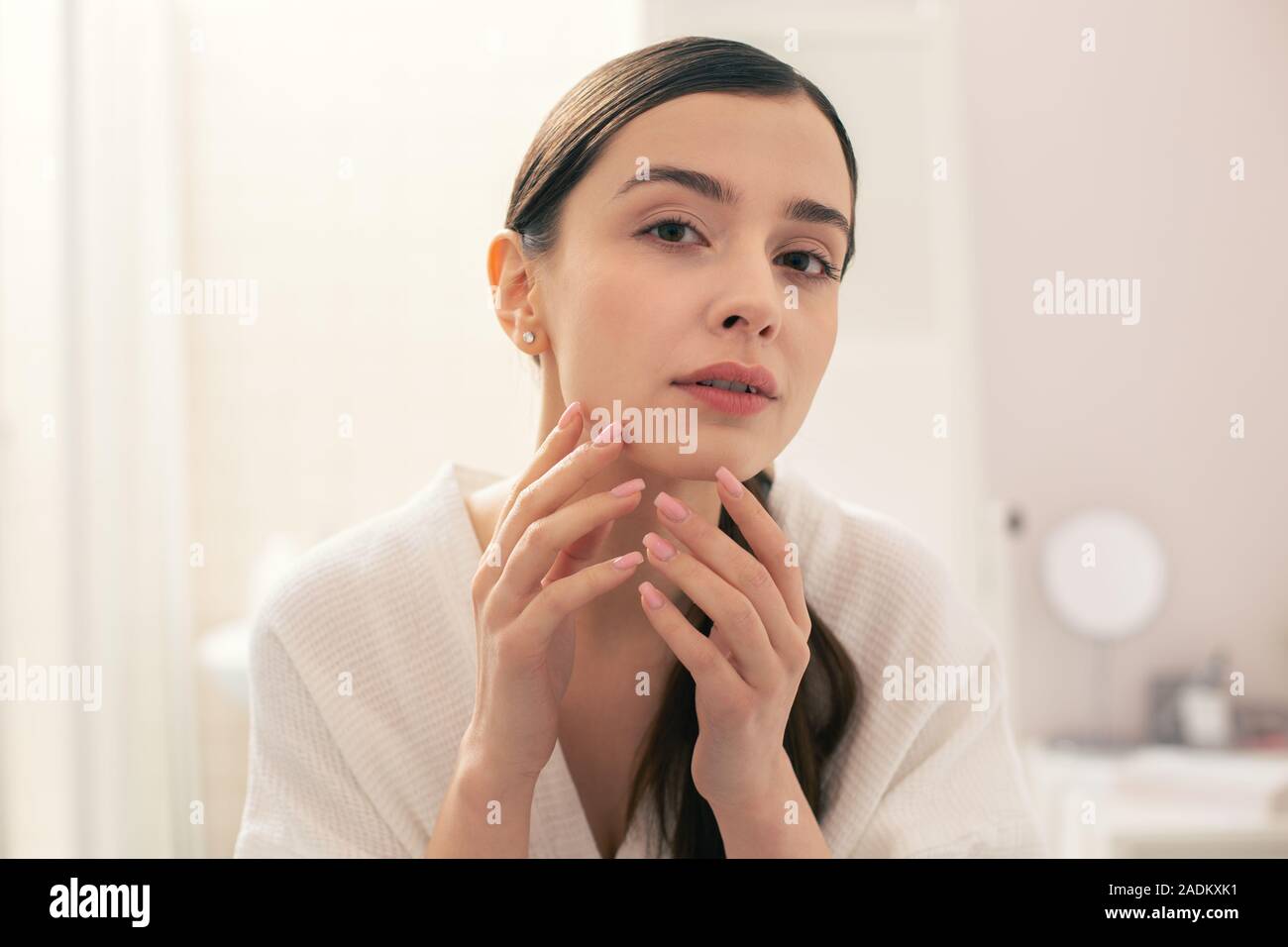 Neugierige Frau, die Ihre Haut analysieren und Ihr Kinn berühren Stockfoto