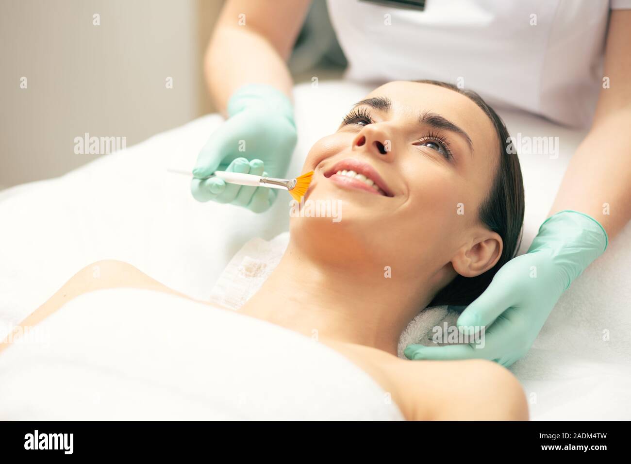 Junge Dame lächelnd, während sie peeling Pinsel cosmetologist Stockfoto