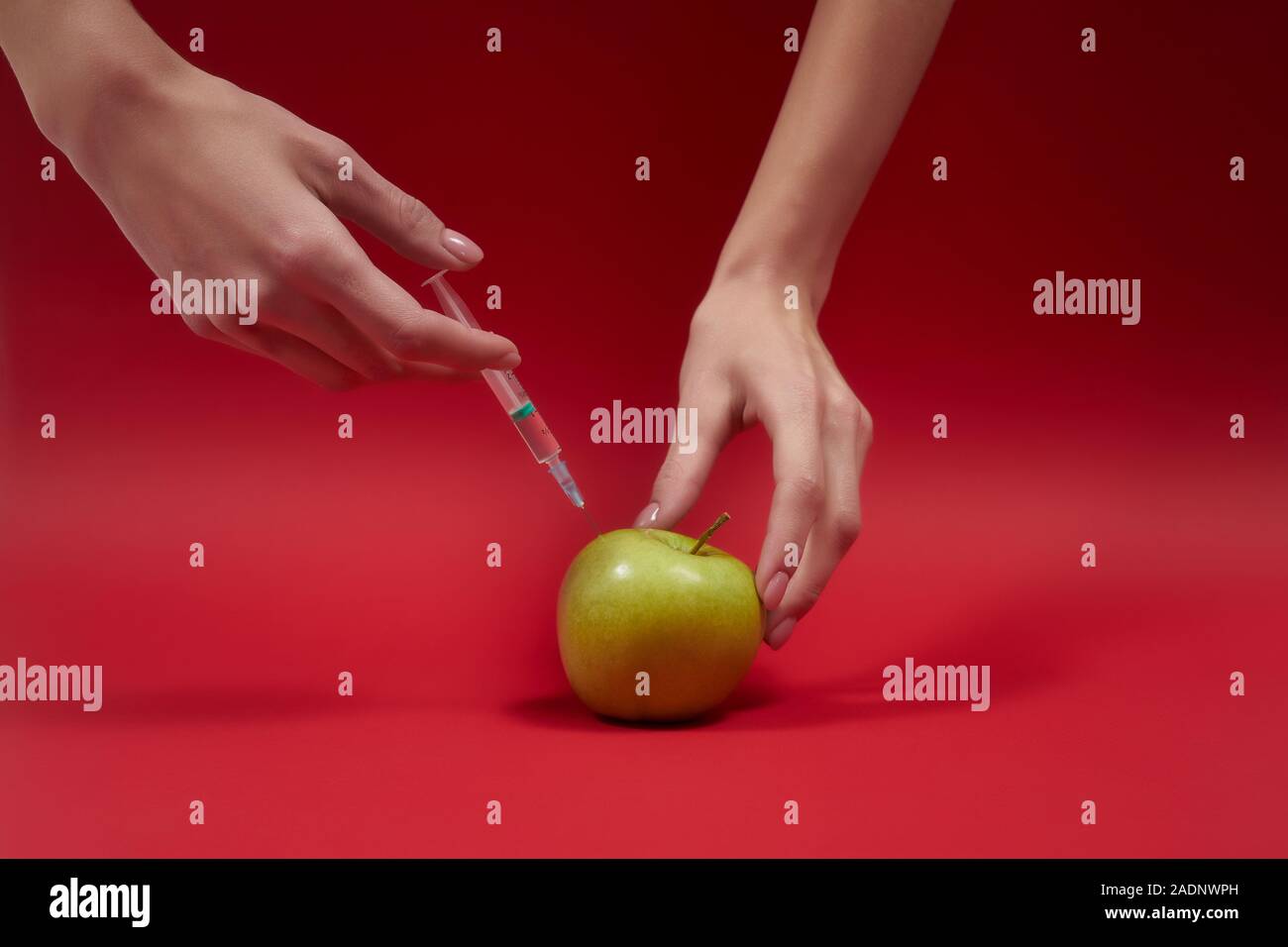 Die Hände der schönen Frau spritzen Gift in den grünen apfel. Spritze mit  Flüssigkeit in Obst. Foto des Konzepts "GMO". Vergiftete Lebensmittel auf  rotem Hintergrund Stockfotografie - Alamy