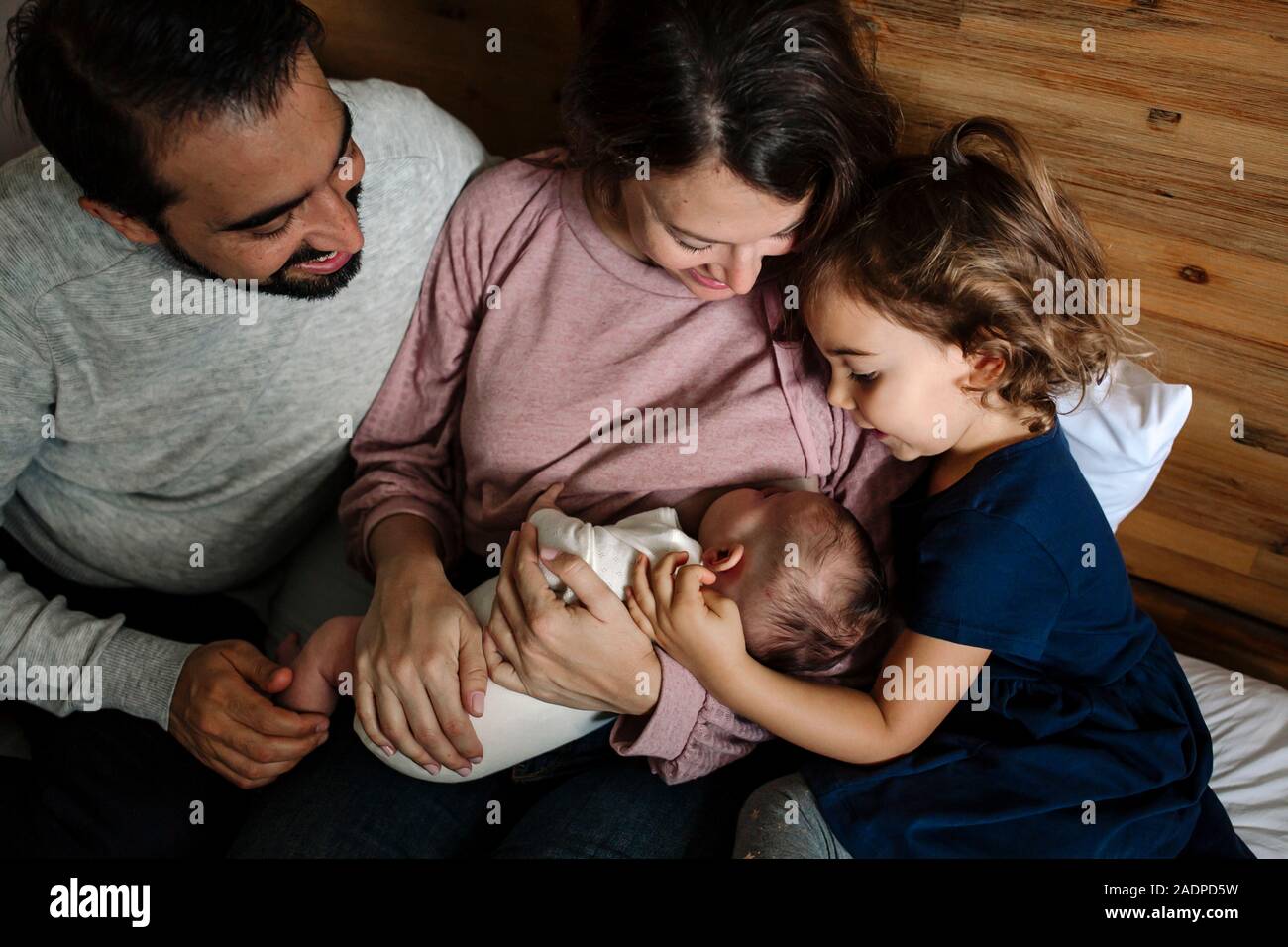 Mama pflege Neugeborene, während Vati und große Schwester ansehen Stockfoto