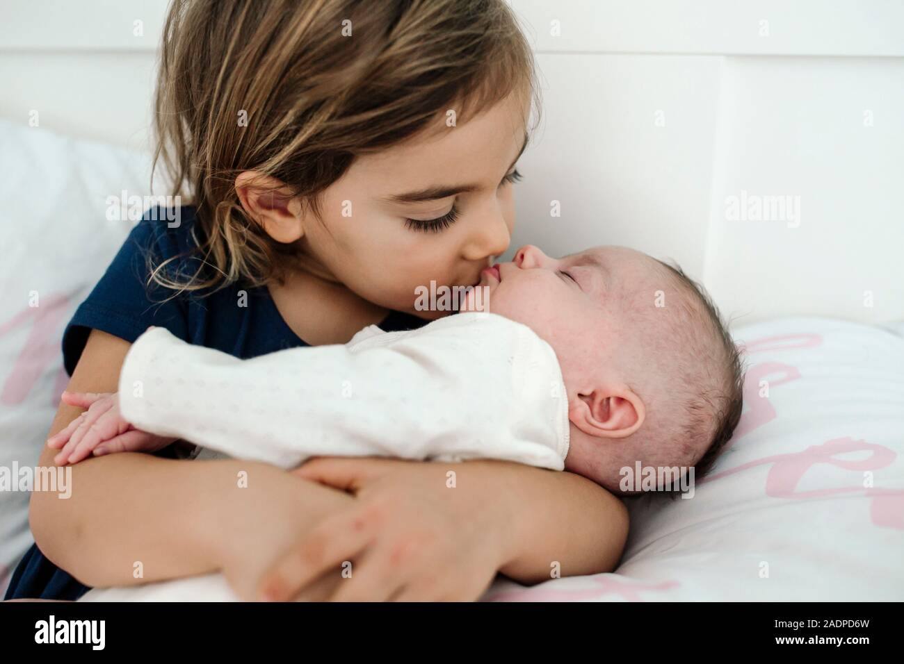 Große Schwester knuddeln und Küssen neugeborenes Geschwister Stockfoto