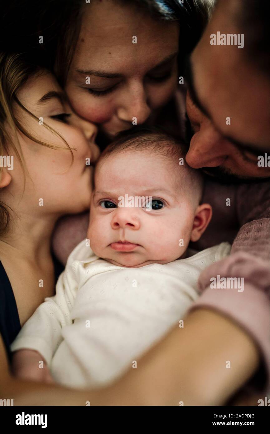 Papa, Mama und große Schwester küssen neugeborenes Baby Stockfoto