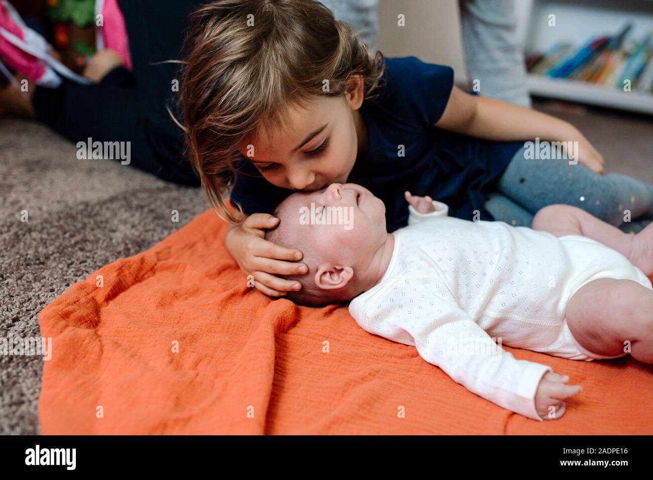 4 Jahre alten küssen Kind Schwester auf orange Decke auf dem Boden Stockfoto