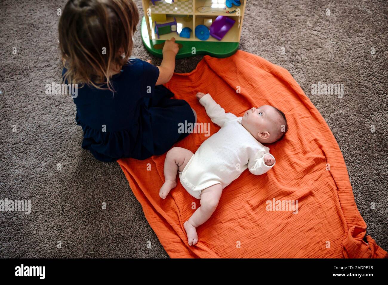 Kleinkind auf orange Decke ansehen Schwester spielen mit Spielzeug Stockfoto