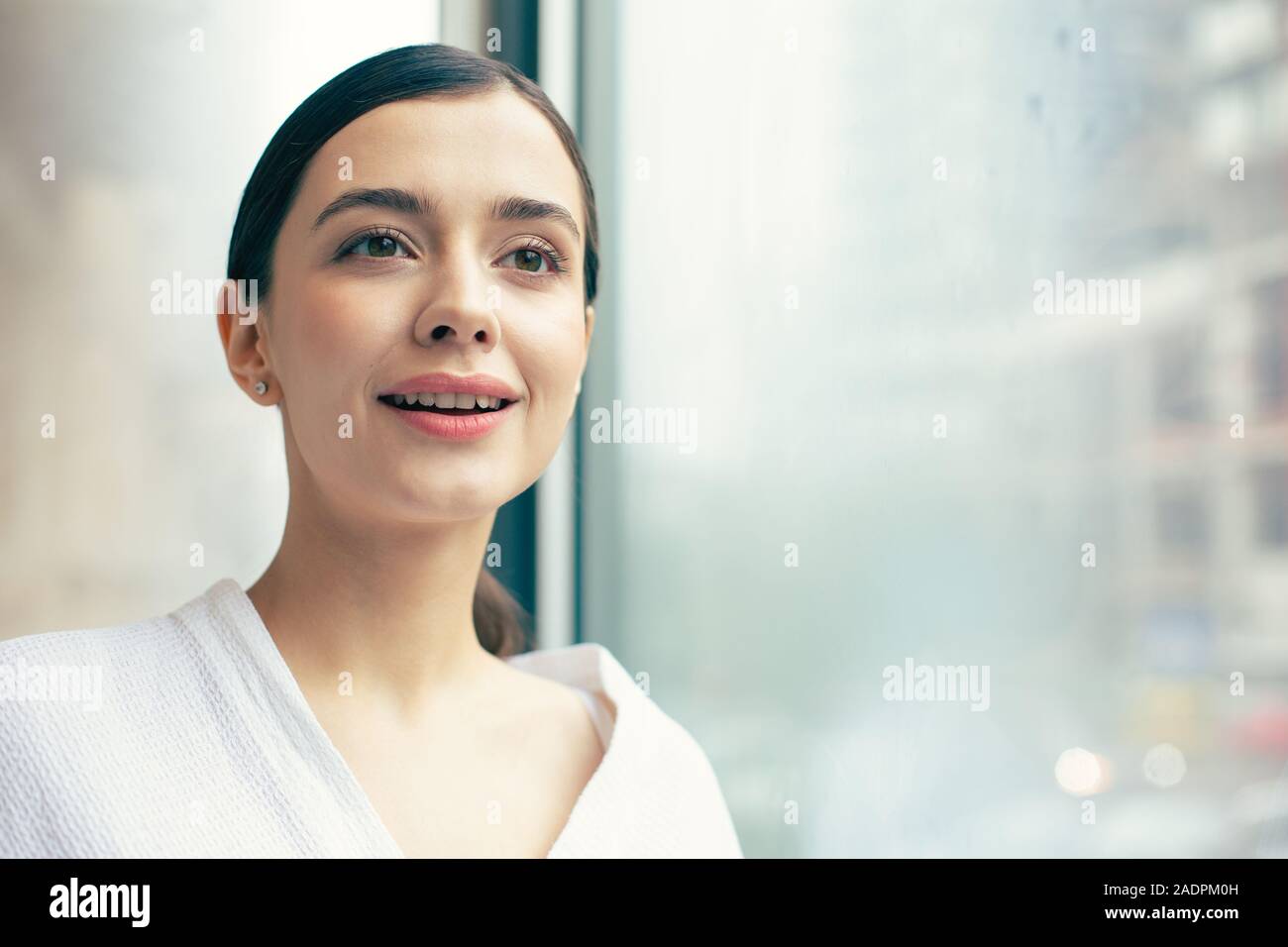 Angesichts des Schönen lächelnde Frau in der Nähe der Fenster aus Glas Stockfoto