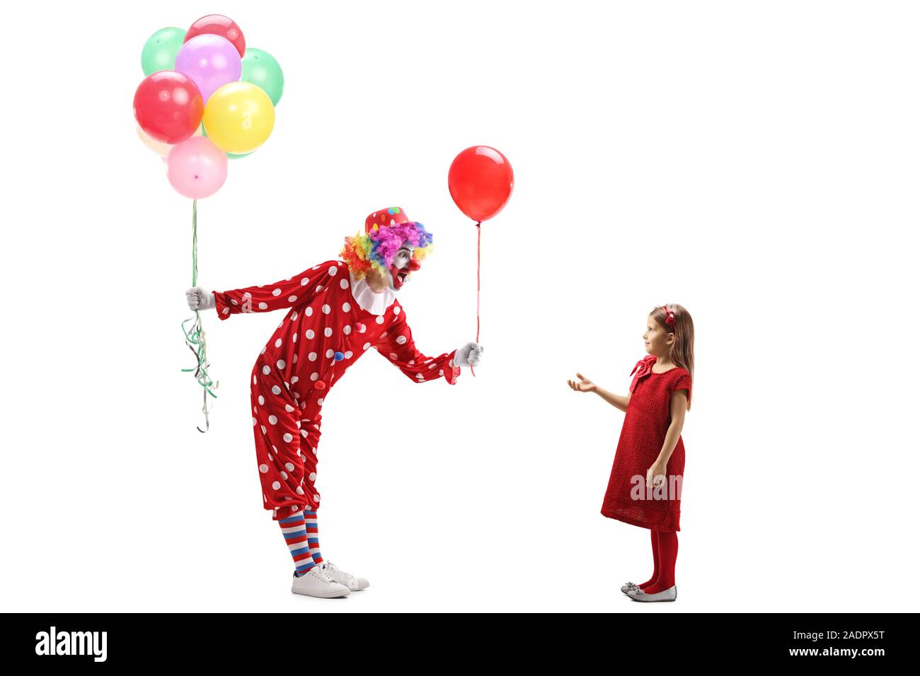 Volle Länge Profil geschossen von einem Clown mit einem Bündel Luftballons mit einem roten Ballon zu einem kleinen Mädchen auf weißem Hintergrund Stockfoto