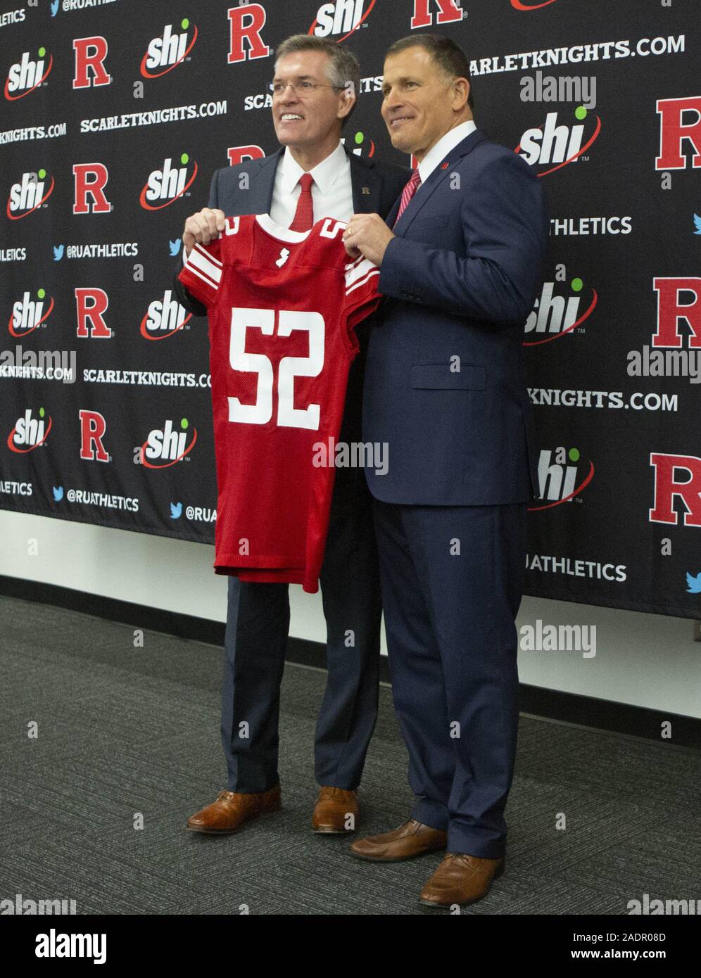 Piscataway, New Jersey, USA. 4. Dez, 2019. Rutgers Athletic Director PATRIC HOBBS wieder Kopf Fußball GRED SCHIANO Hold up Trainer Eric LeGrands "Jersey während einer Pressekonferenz bei der Ankündigung der Schiano zurück im Hale Centre in Piscataway, New Jersey zurückzog. Credit: Brian Zweig Preis/ZUMA Draht/Alamy leben Nachrichten Stockfoto