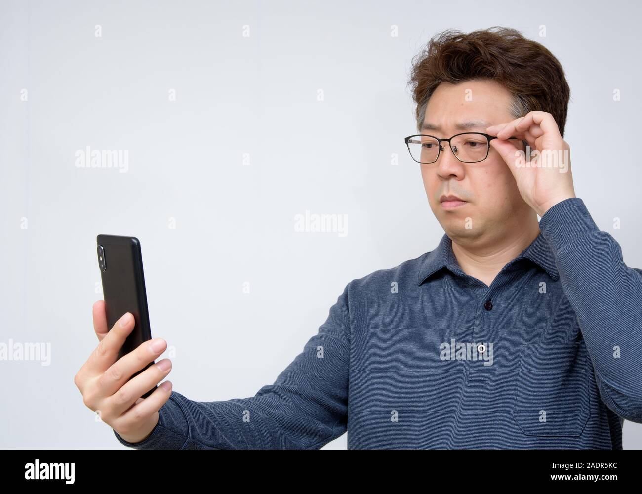 Asiatische Männer, die versuchen, etwas auf seinem Handy zu lesen. schlechte Sicht, alterssichtigkeit, Kurzsichtigkeit. Stockfoto