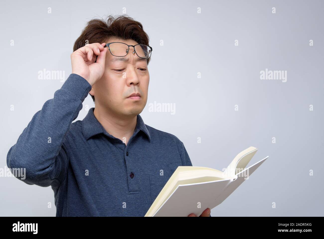 Asiatische Männer versuchen, etwas in seinem Buch zu lesen. schlechte Sicht, alterssichtigkeit, Kurzsichtigkeit. Stockfoto